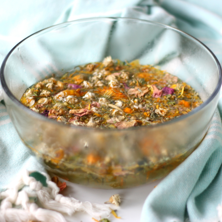 a glass bowl full of water and floating floral herbs surrounded by a turquoise cotton towel.
