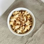 A white bowl filled to the brim with pumpkin spices popcorn on a khaki cloth background.