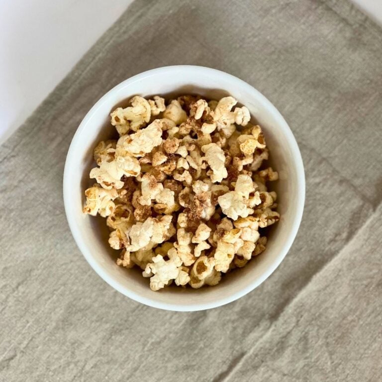 A white bowl filled to the brim with pumpkin spices popcorn on a khaki cloth background.