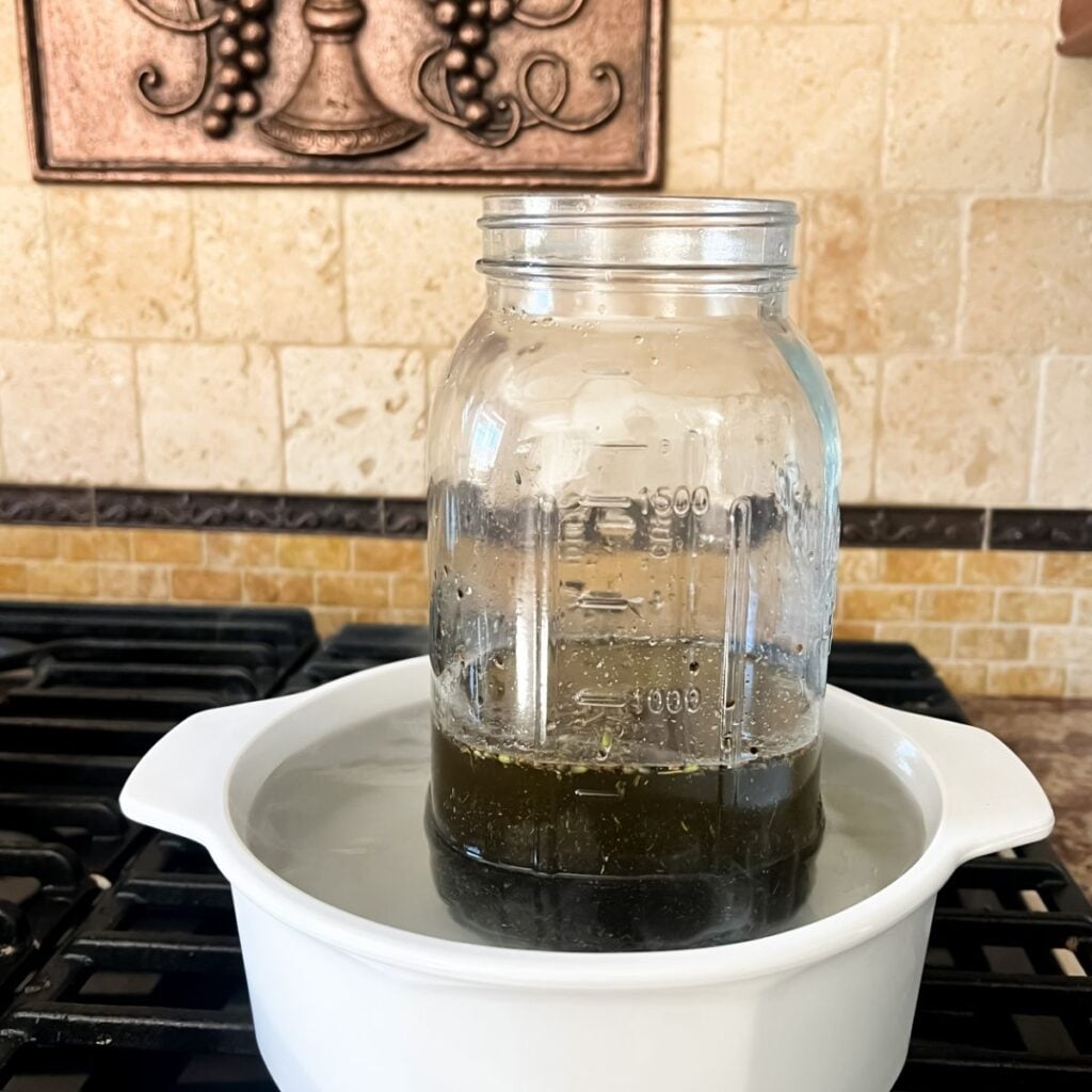 A large mason jar willed with olive oil and ground lavender buds in a double boiler.
