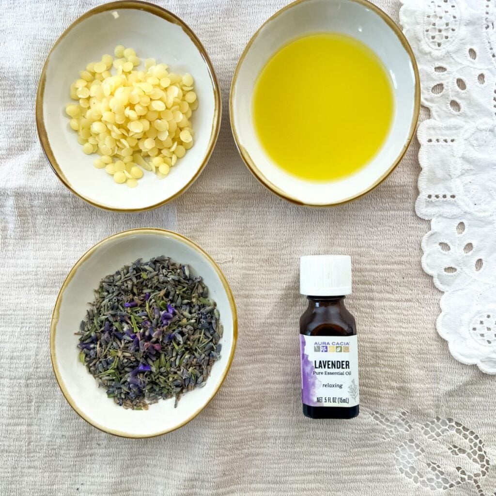 three small bowls filled with the ingredients for the lavender salve and a bottle of lavender essential oil. 